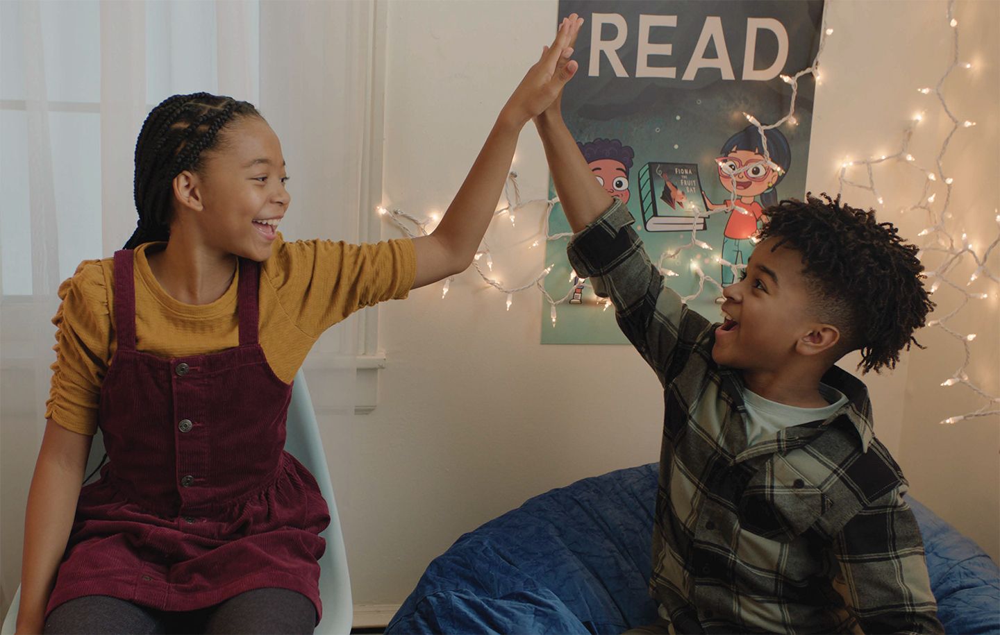 two kids high-fiving each other in front of a poster on the wall that says READ